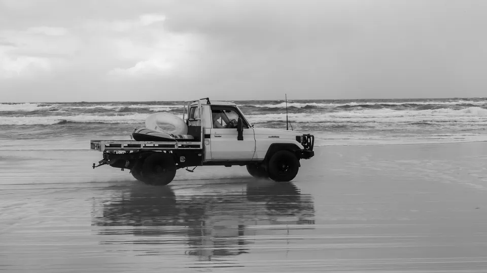 Black and white photograph of a four wheel drive on wet sand flats
