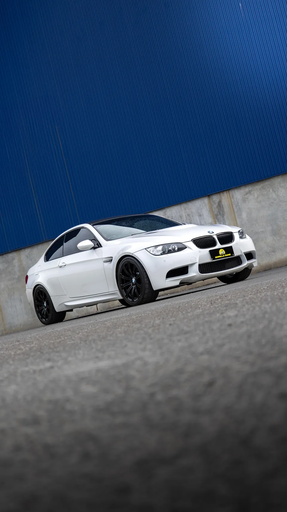 White BMW M3 photographed side-on against a blue industrial wall