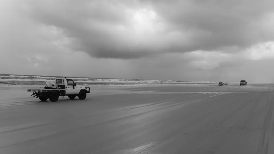 Black and white wide shot of vehicles on distant tidal flats