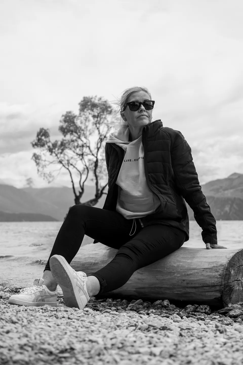 Black and white portrait of a woman seated on a log by a lake
